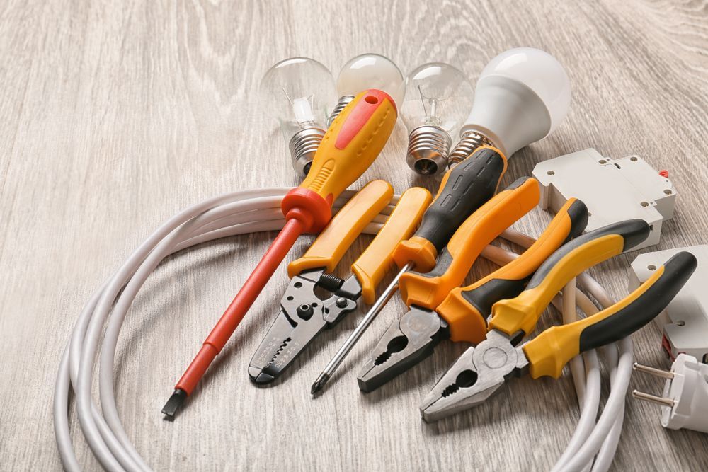 Electrician Tools Including Screwdrivers, Pliers, Wires, and Lightbulbs on a Wooden Surface — Holders Electrical In Inverell, NSW