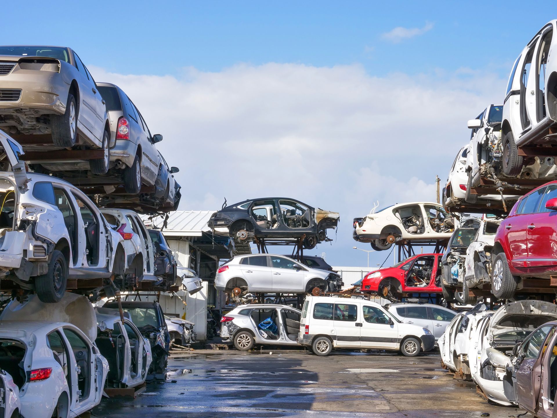 Stacks of crushed cars in an outdoor auto scrapyard under a blue sky