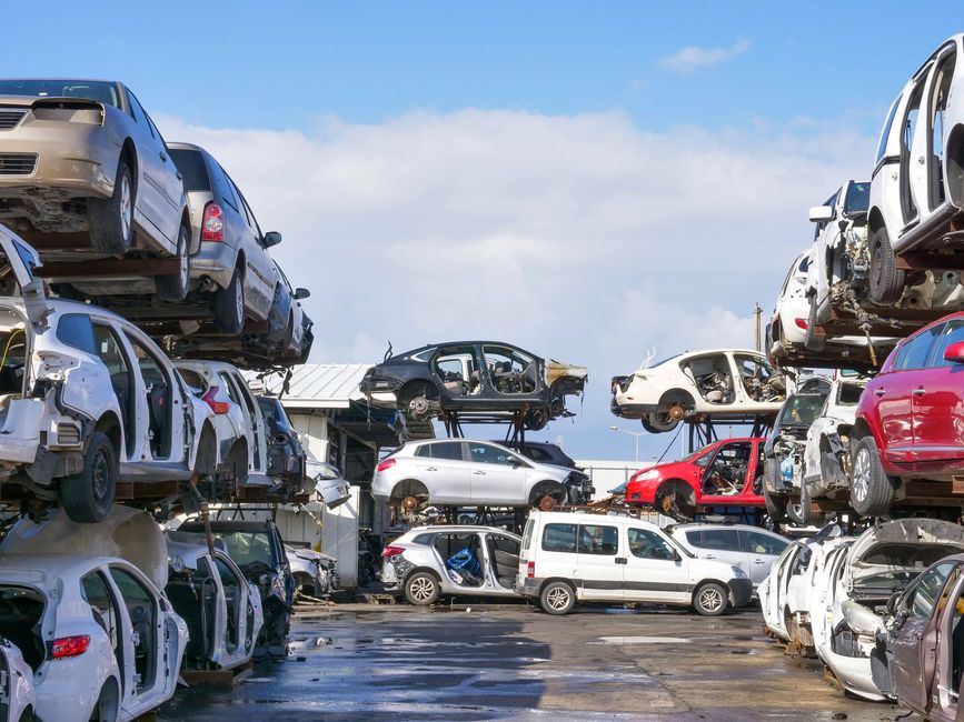 Stacks of crushed cars in an outdoor auto scrapyard under a blue sky