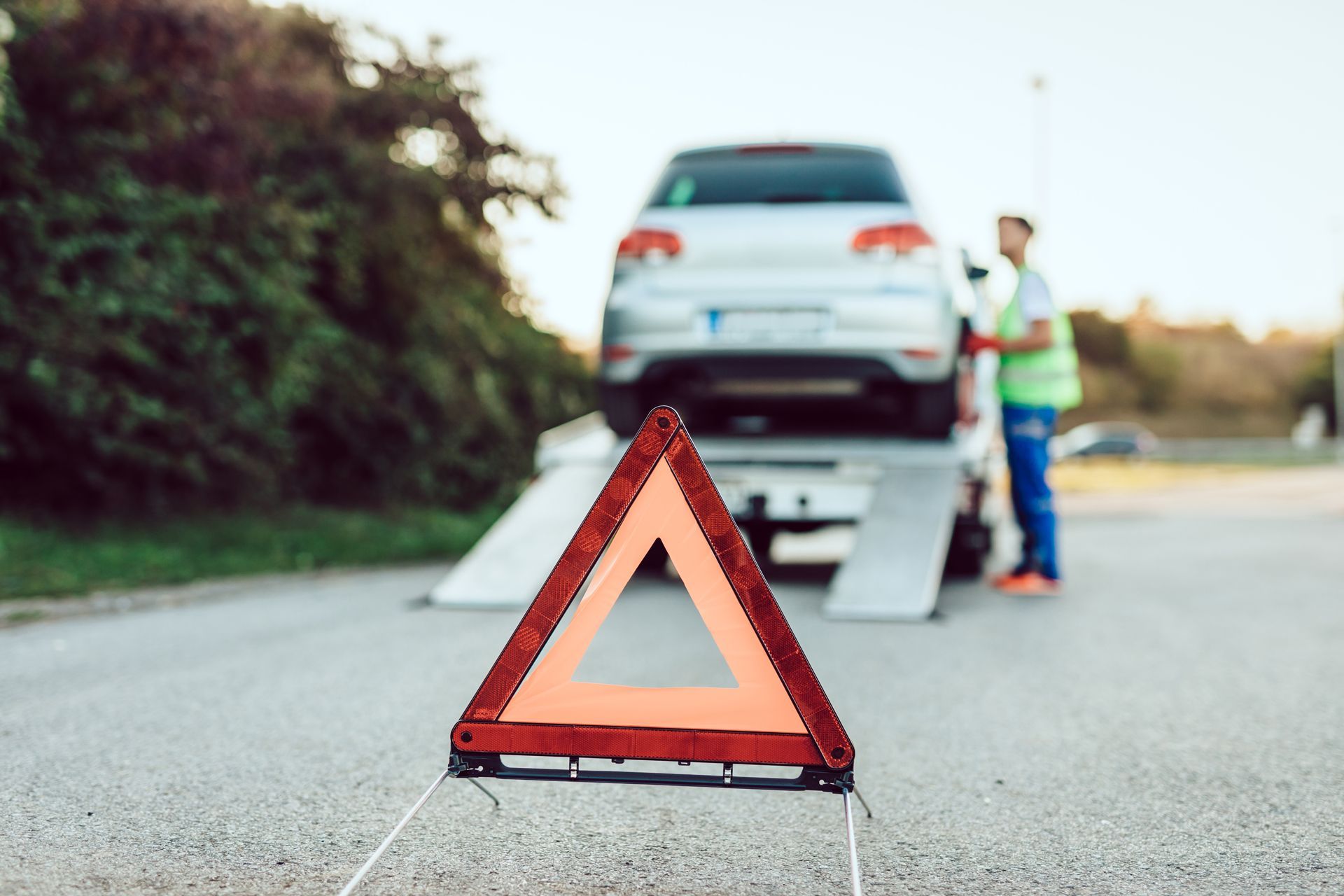 Red warning triangle on road behind a car on a tow truck, with a worker nearby