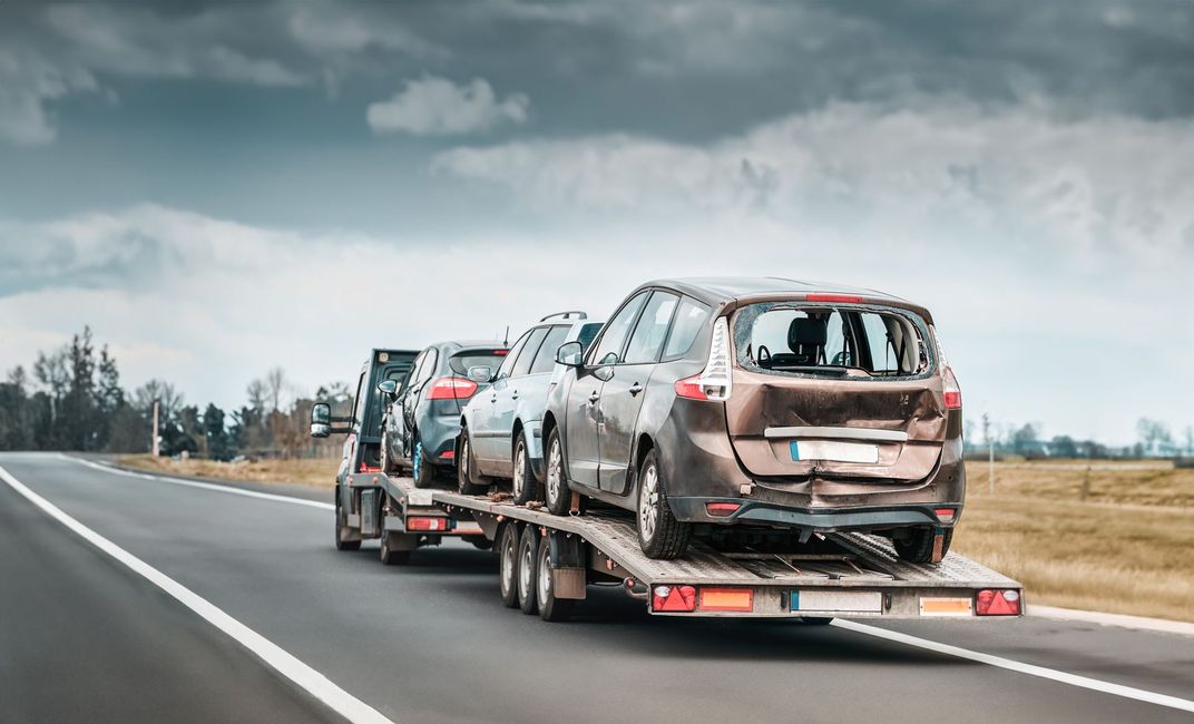 Car carrier trailer hauling damaged cars on a highway under cloudy skies