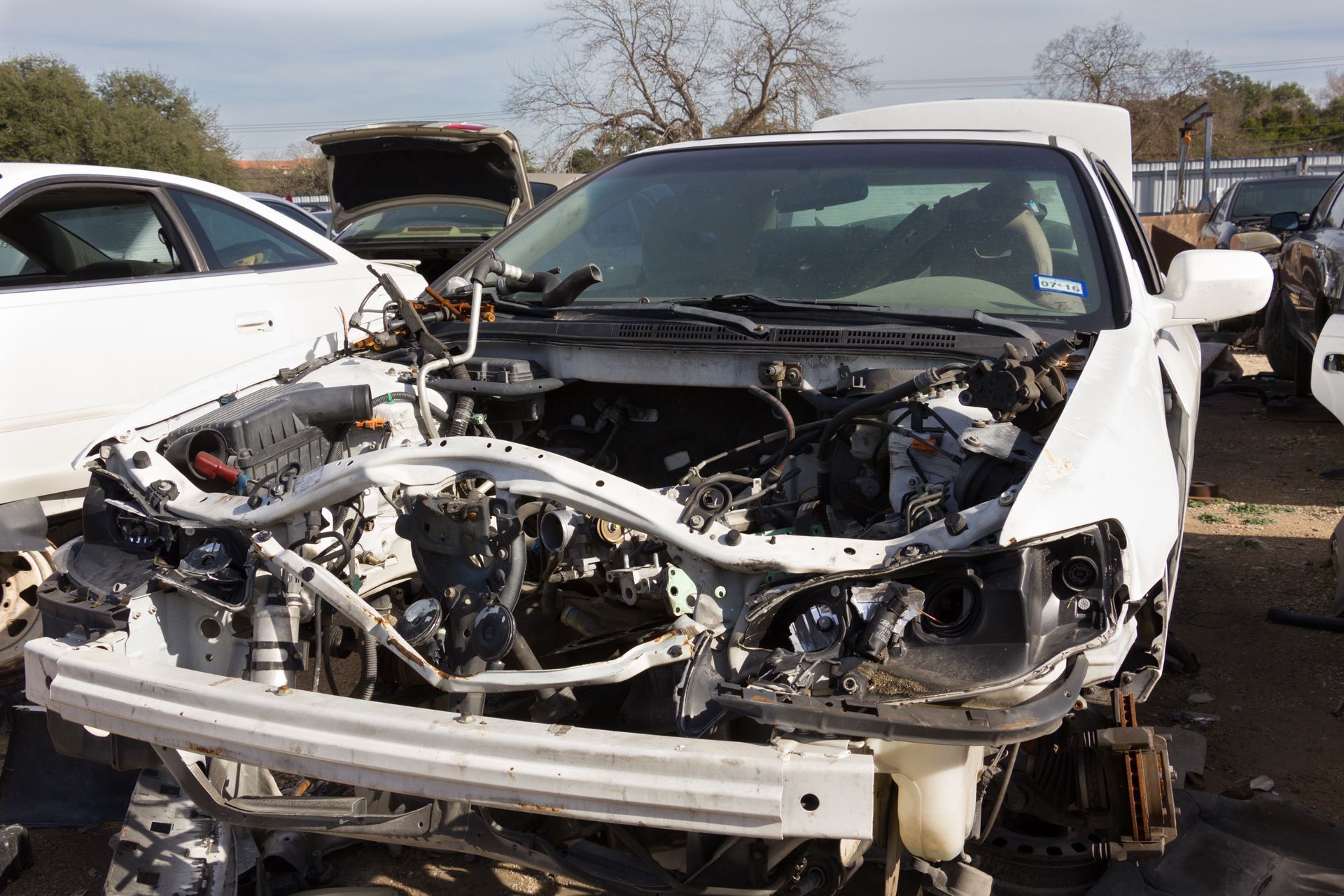 Severely damaged white car with front end exposed in a junkyard or salvage lot