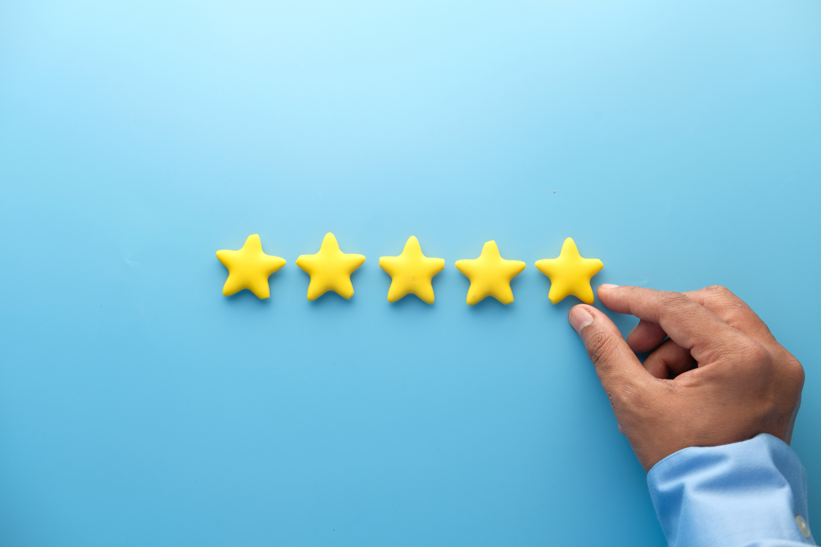 Hand placing a fifth gold star in a 5-star rating on a blue background