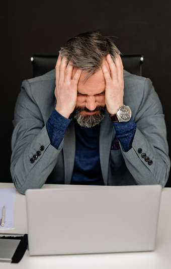 Stressed man at desk with laptop, holding his head in his hands