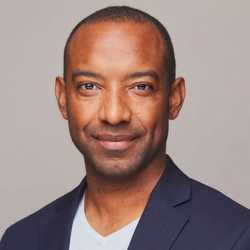 A man in a suit and white shirt is smiling for the camera.