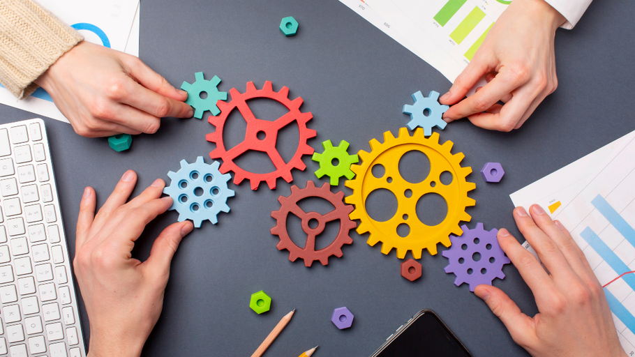 Hands arranging colorful gear-shaped puzzle pieces on a desk with charts and a keyboard.