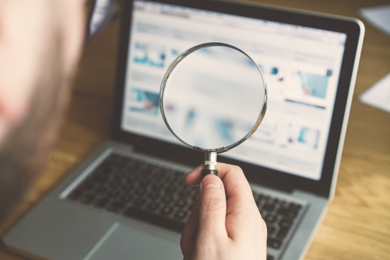 Hand holding a magnifying glass over a laptop screen displaying blurred search results