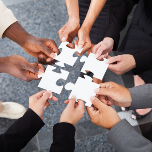Hands of various people holding puzzle pieces, connecting to complete the puzzle.