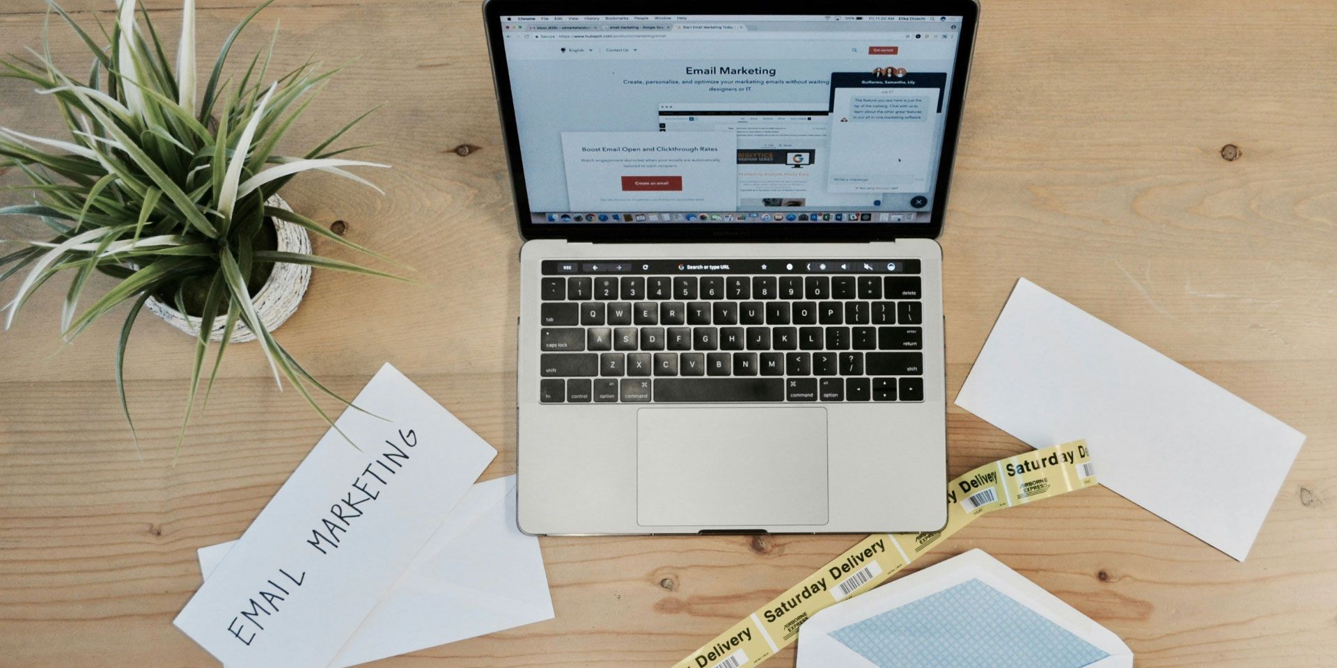Overhead view of laptop on wooden desk with plant, papers, notebook, and coffee cup
