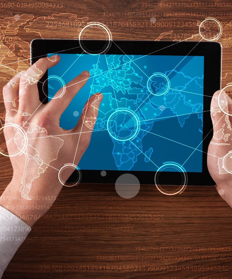 Hands using a tablet on a wooden table with a blue digital network display