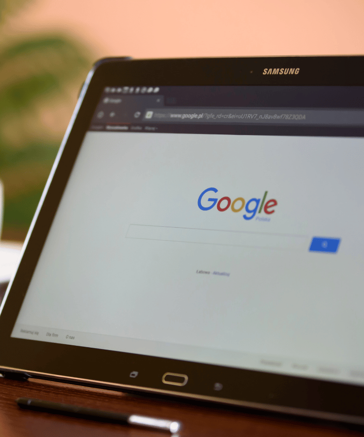 Tablet displaying the Google homepage on a desk, with a blurred background