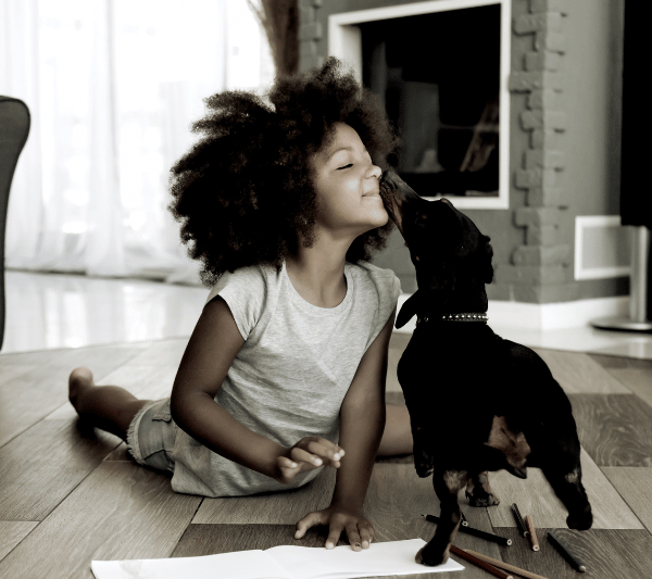 A little girl is sitting on the floor with her dog