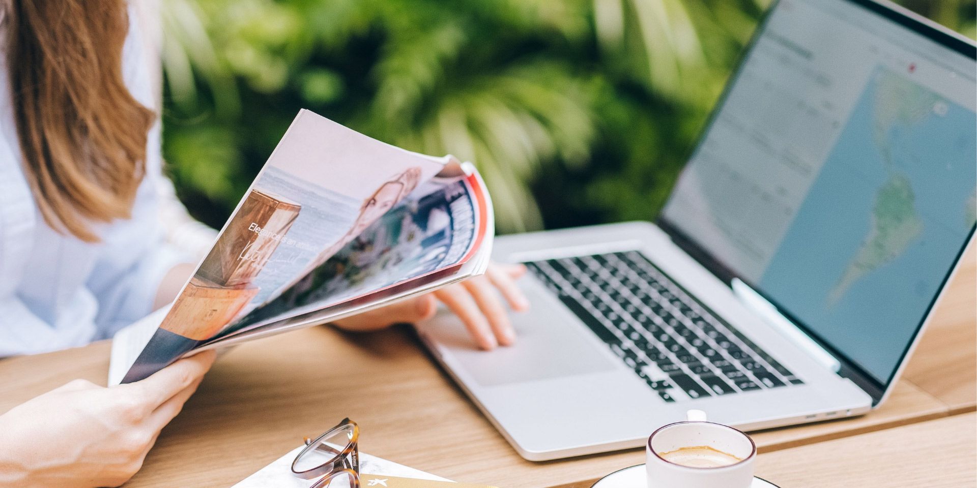 Person reviewing printed materials beside a laptop at a desk outdoors