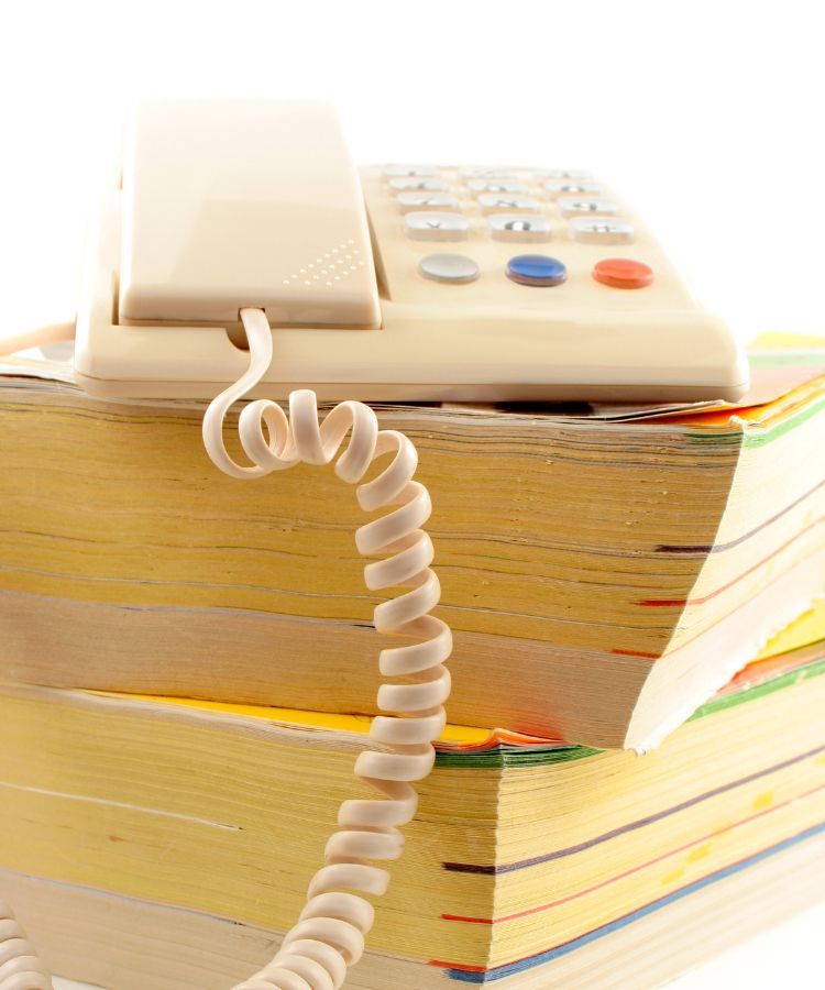 White landline phone on stacked books with a coiled cord hanging down