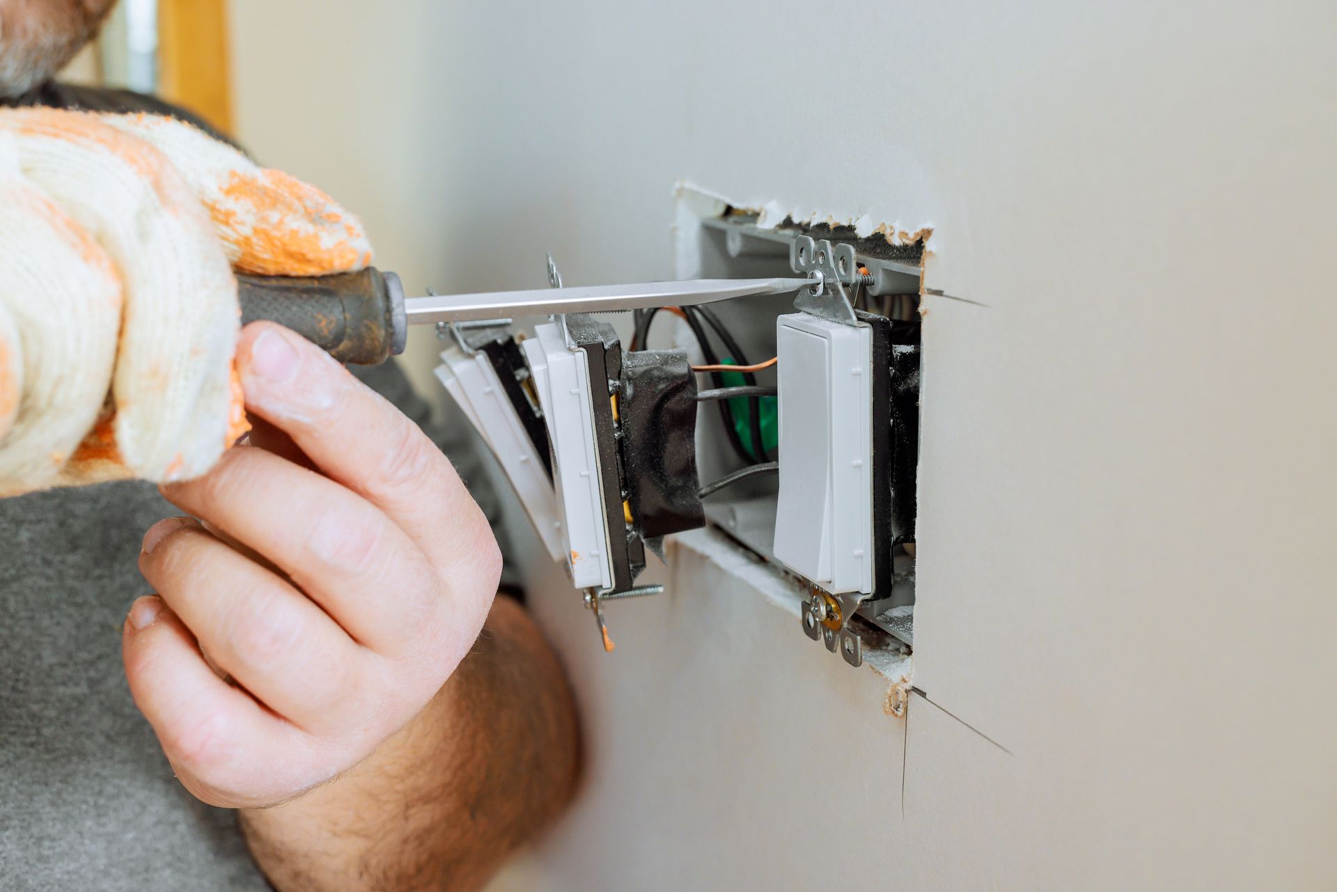 Hand installing an electrical switch into a wall outlet box with exposed wiring.
