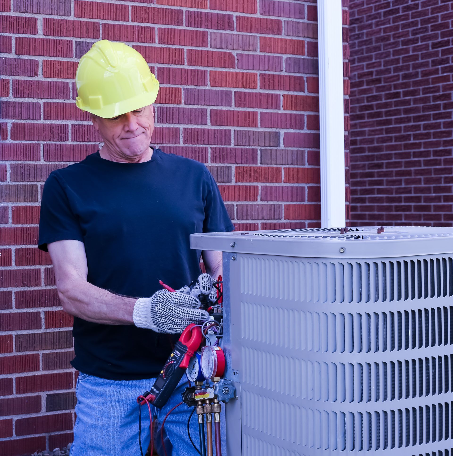Worker in hard hat handling HVAC equipment beside a brick wall
