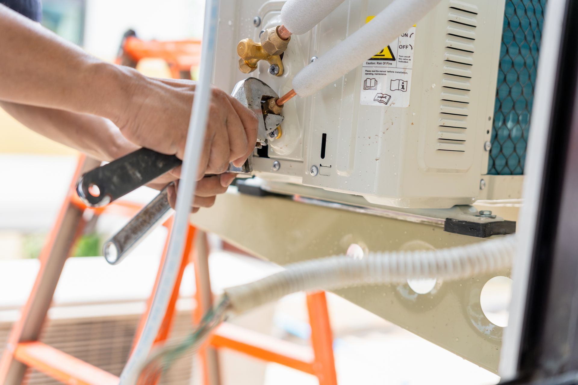 Person using tools to repair an outdoor air conditioner unit on a ladder