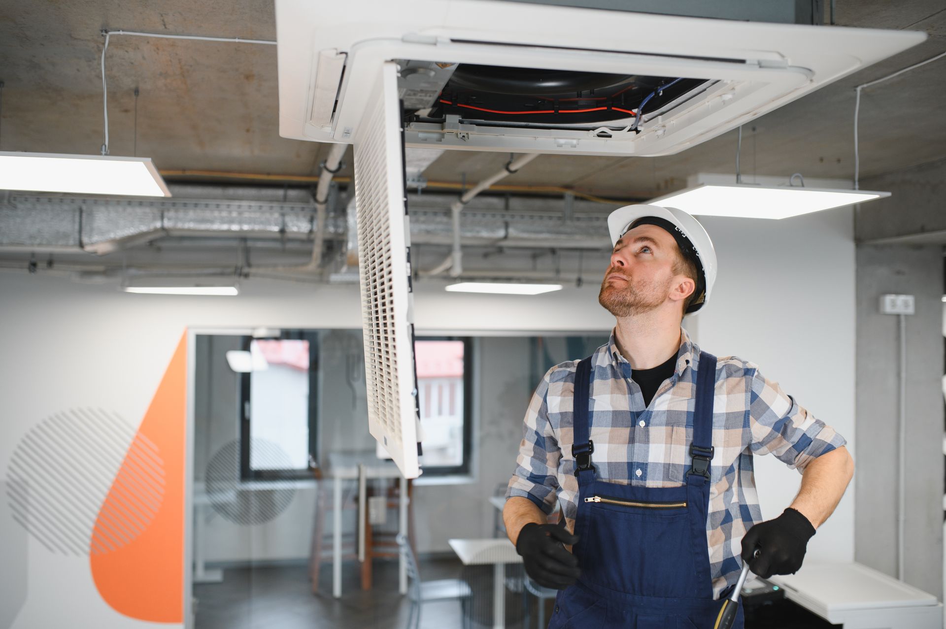 Technician inspecting a ceiling HVAC unit in an office interior