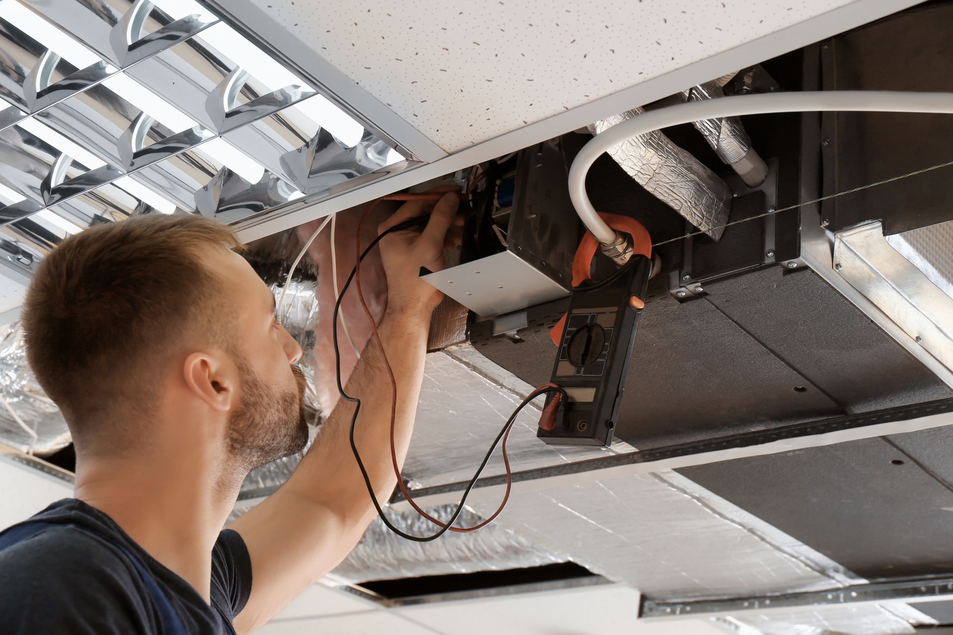Technician installing wiring in a drop ceiling with a drill and exposed ceiling tiles