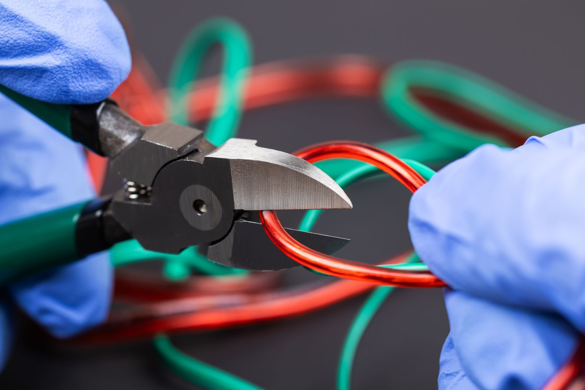 Gloved hands use wire cutters to trim red and green electrical wires
