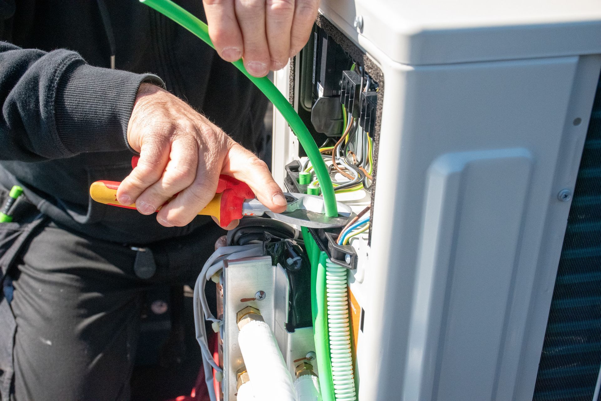 Technician wiring a utility box with green cables and pliers outdoors