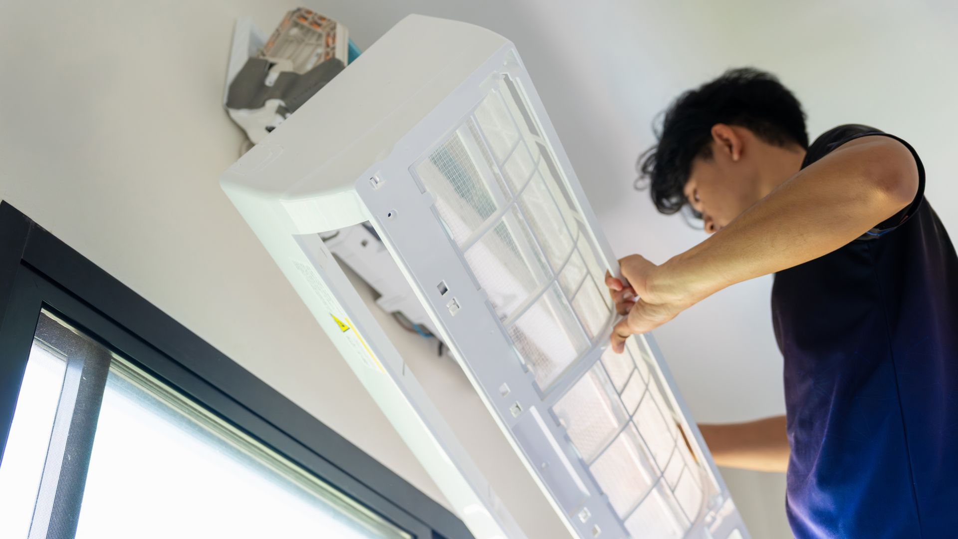 Person installing a white air conditioner on a wall near a window.