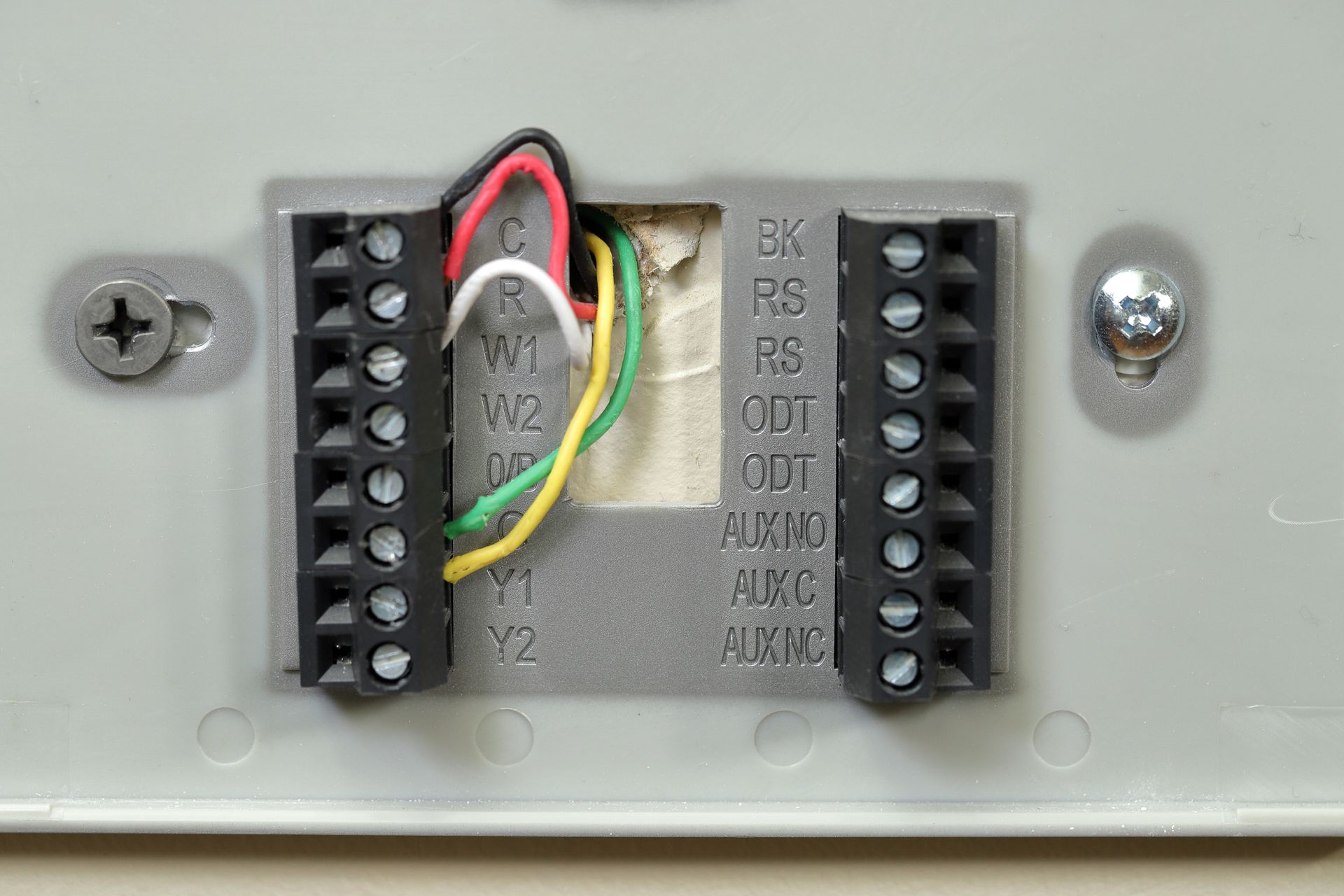 Close-up of a device terminal block with black screw connectors and red, yellow, and green wires attached