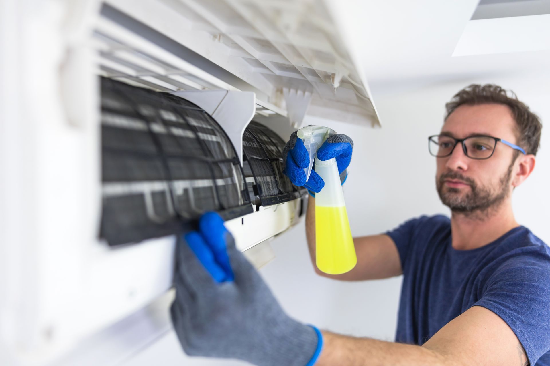 Technician cleaning a wall-mounted air conditioner with a spray bottle and cloth