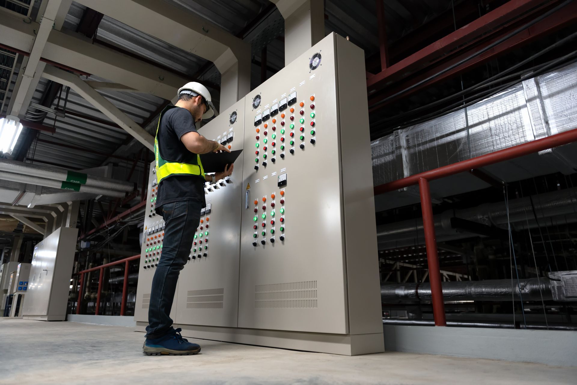 Worker in hard hat operating a large control panel in an industrial facility.