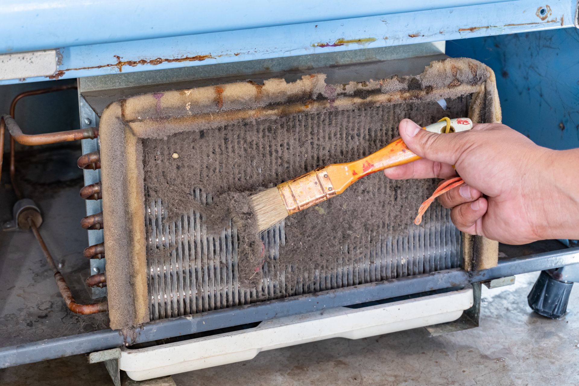 Hand brushing dust from a dirty HVAC filter on a blue unit