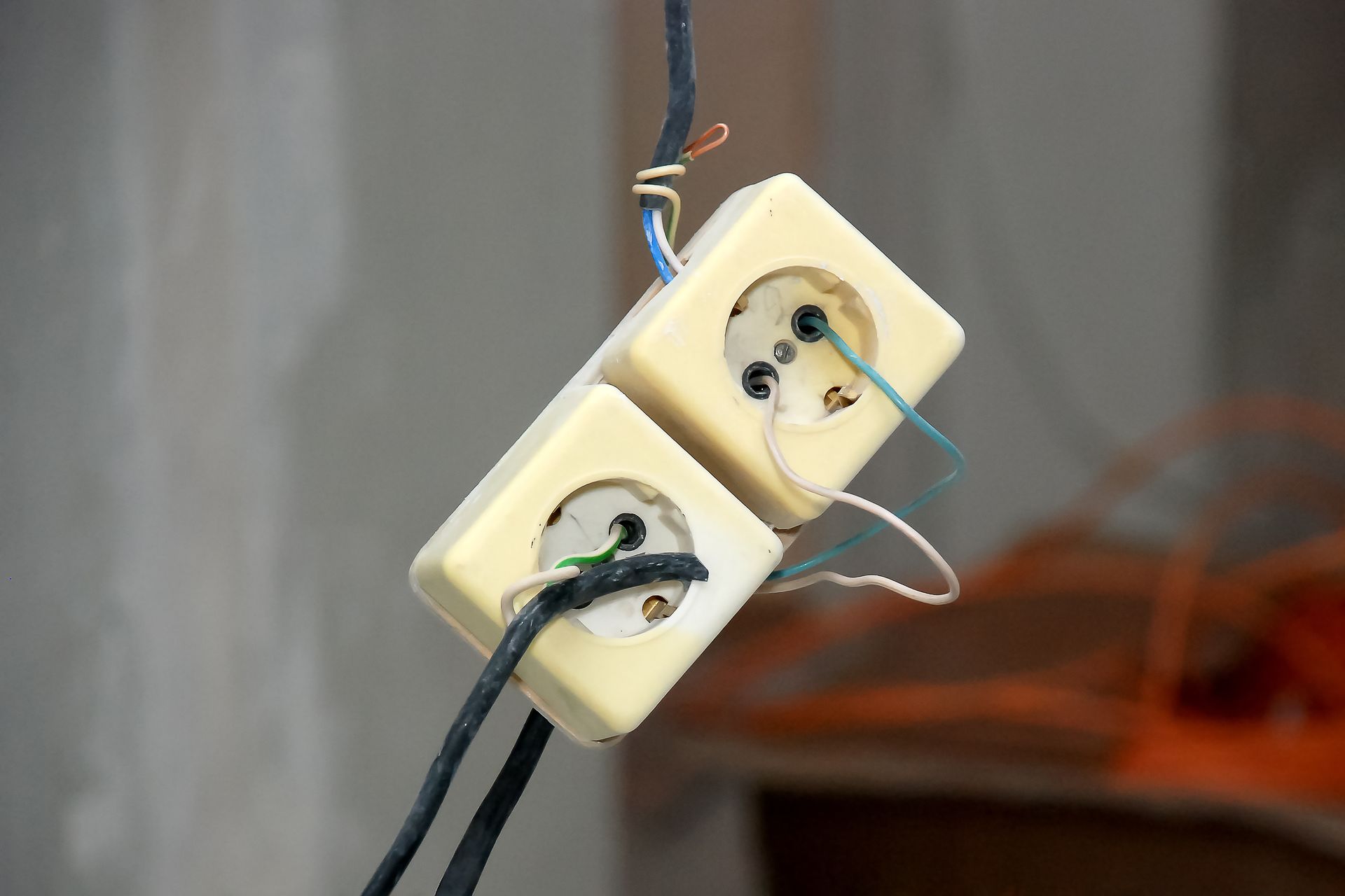 Two electrical outlets with exposed wires and a black cable, suspended against a gray background