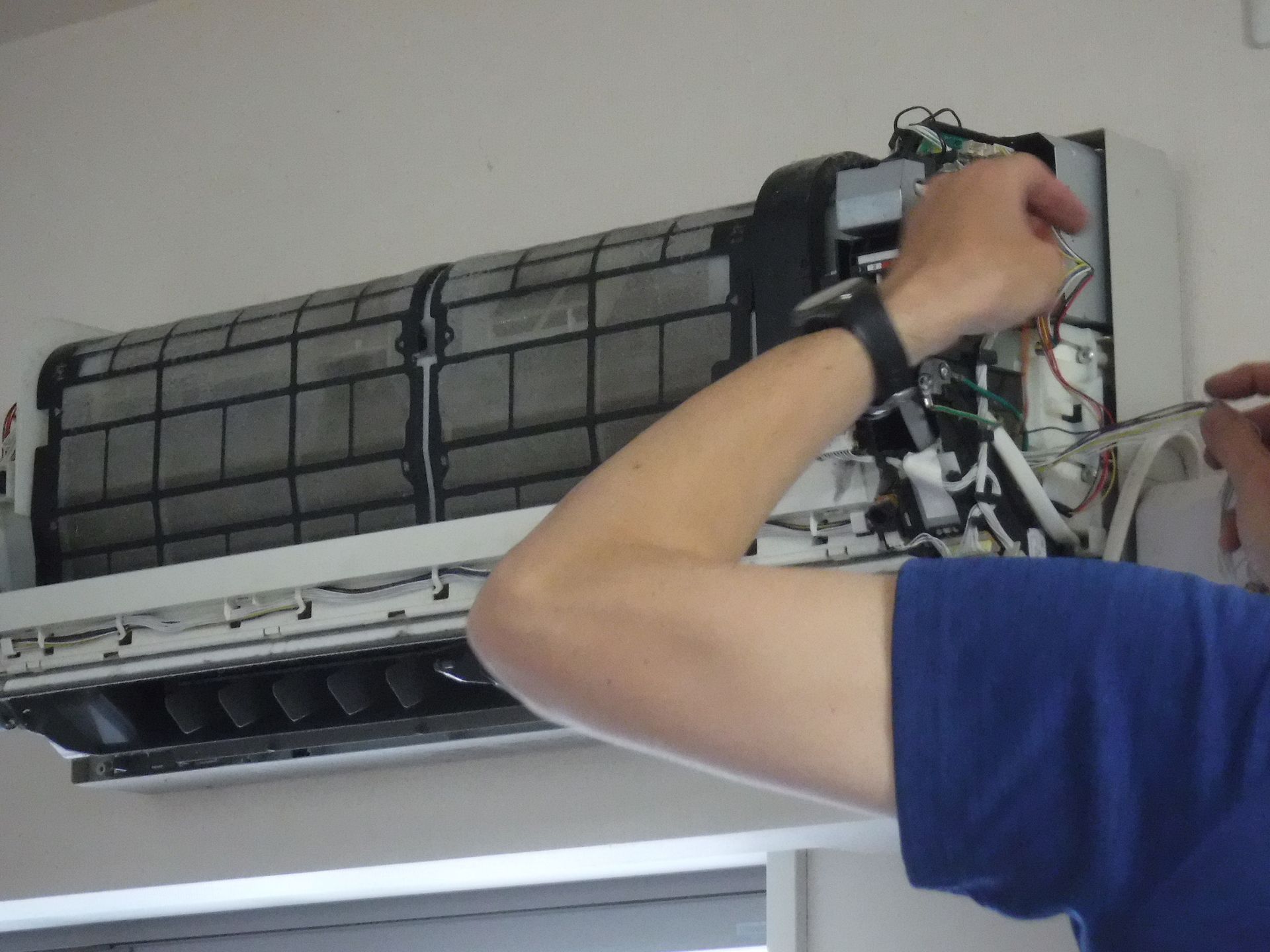 Person repairing a wall-mounted air conditioner with tools.