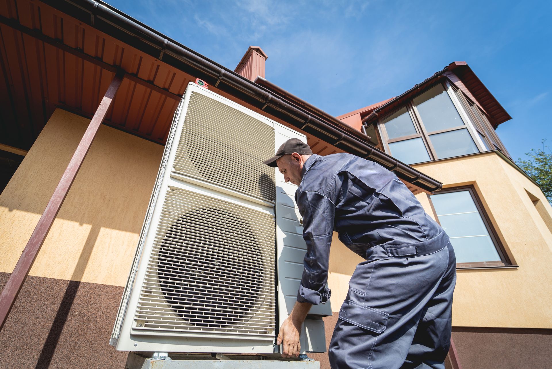 Technician inspecting a house’s outdoor air conditioner unit beside a window