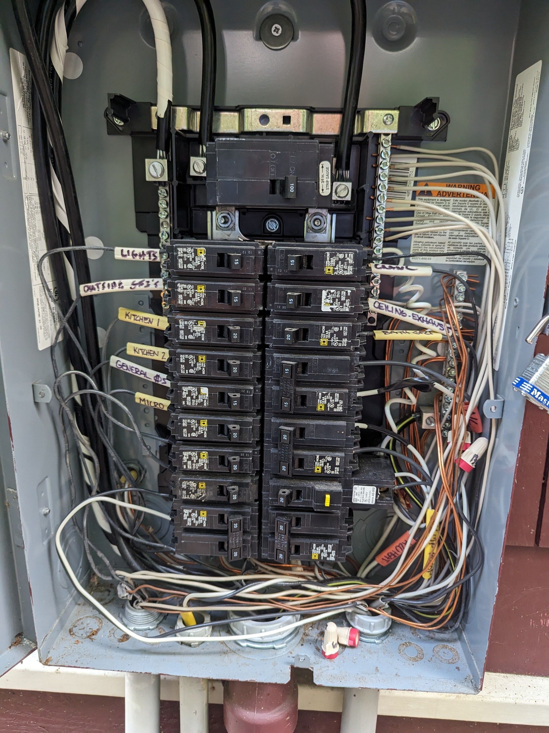Open electrical breaker panel with multiple black circuit breakers and exposed wiring