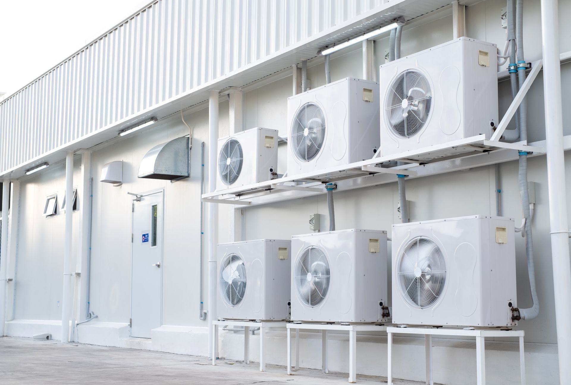 Row of outdoor air conditioning units mounted along a white building wall