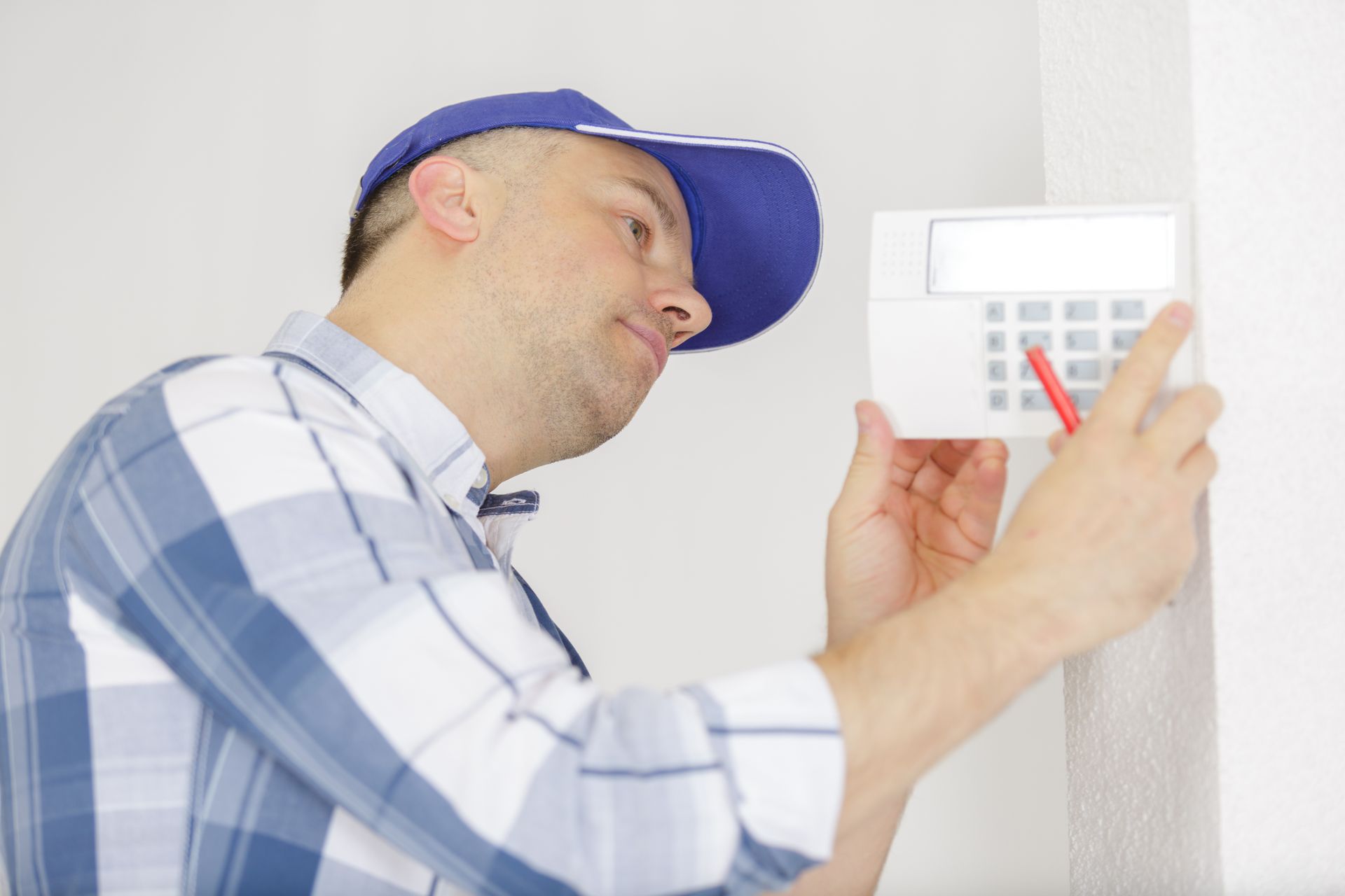 Man in blue cap checking a wall-mounted security keypad with a red indicator light