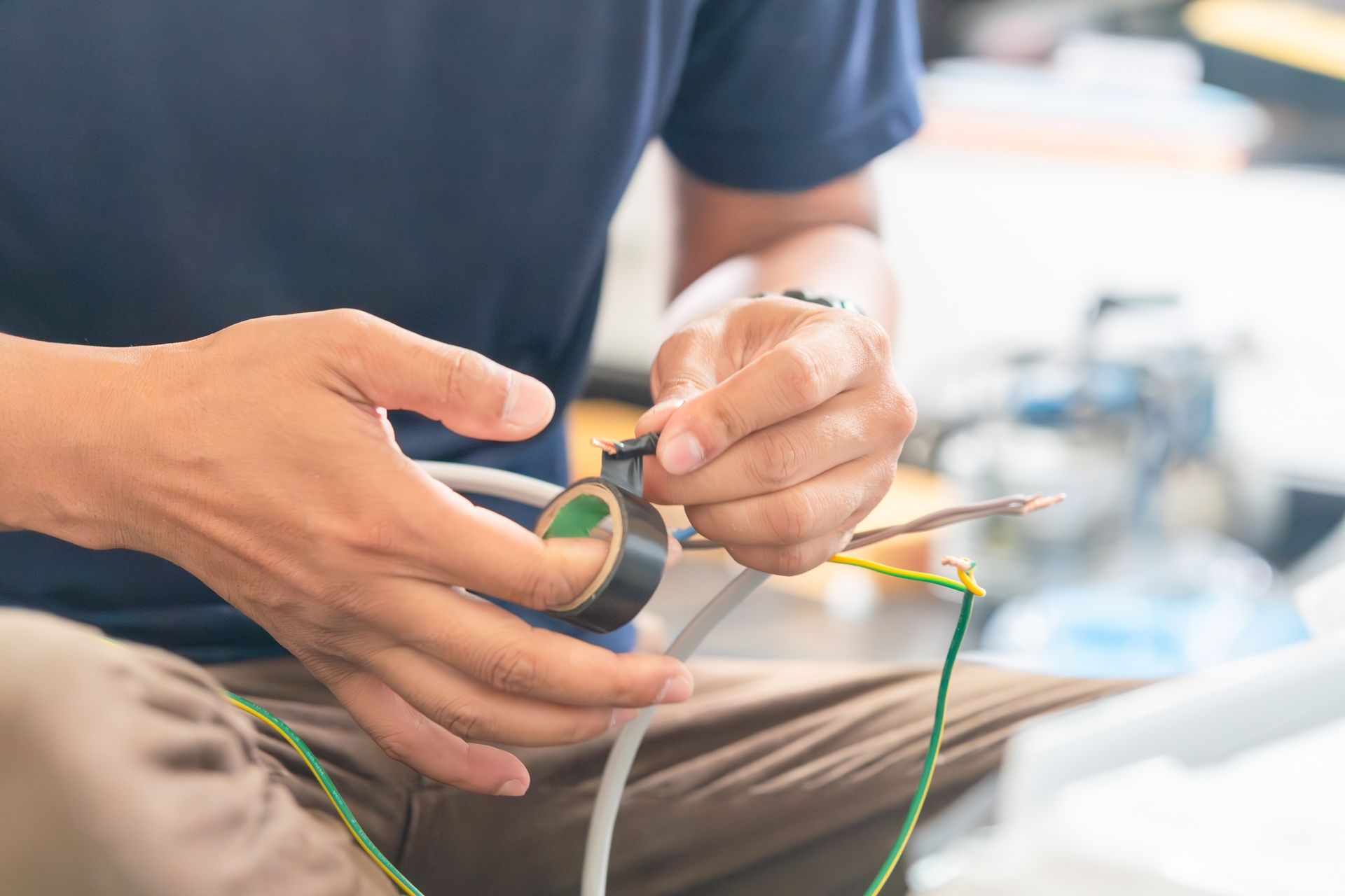 Hands threading green wire through a small black ring in a close-up workbench scene