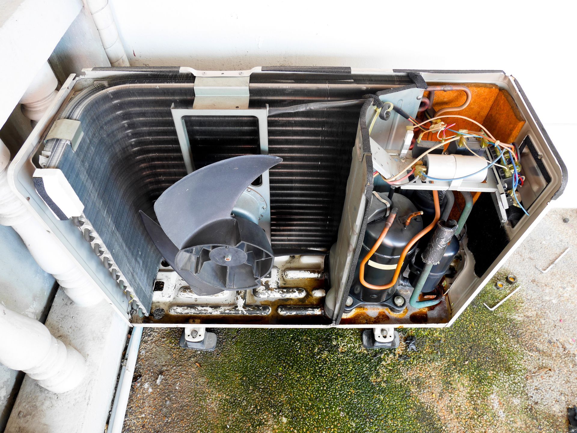 Open HVAC unit with exposed coils, fan, and wiring on a concrete surface.