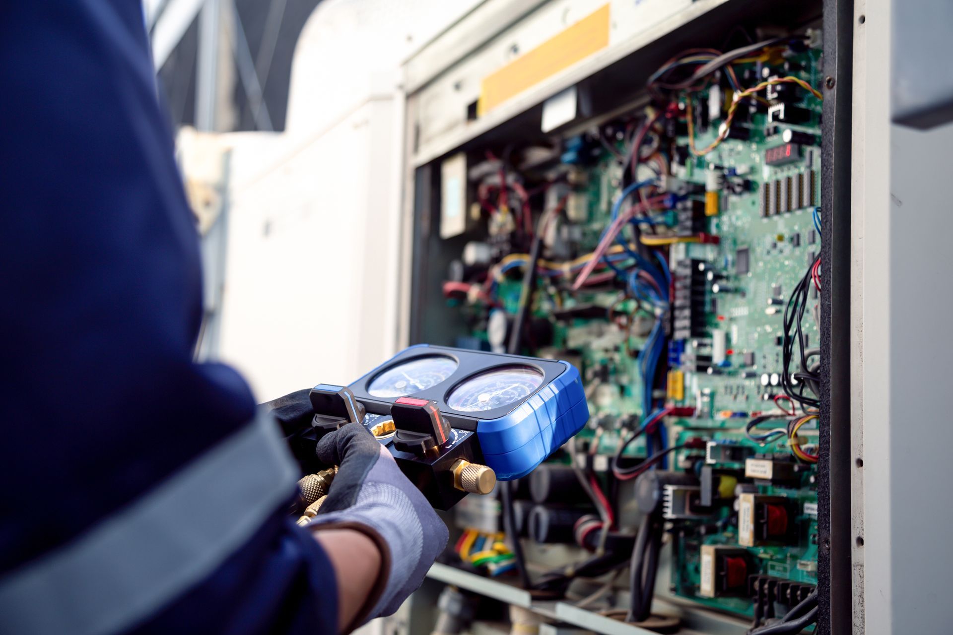 Technician in gloves inspecting wiring inside an open electrical control cabinet with a blue tool箱