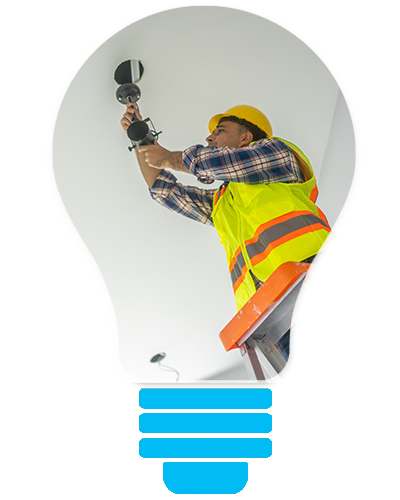 Electrician in yellow safety vest installing a light bulb in a ceiling fixture