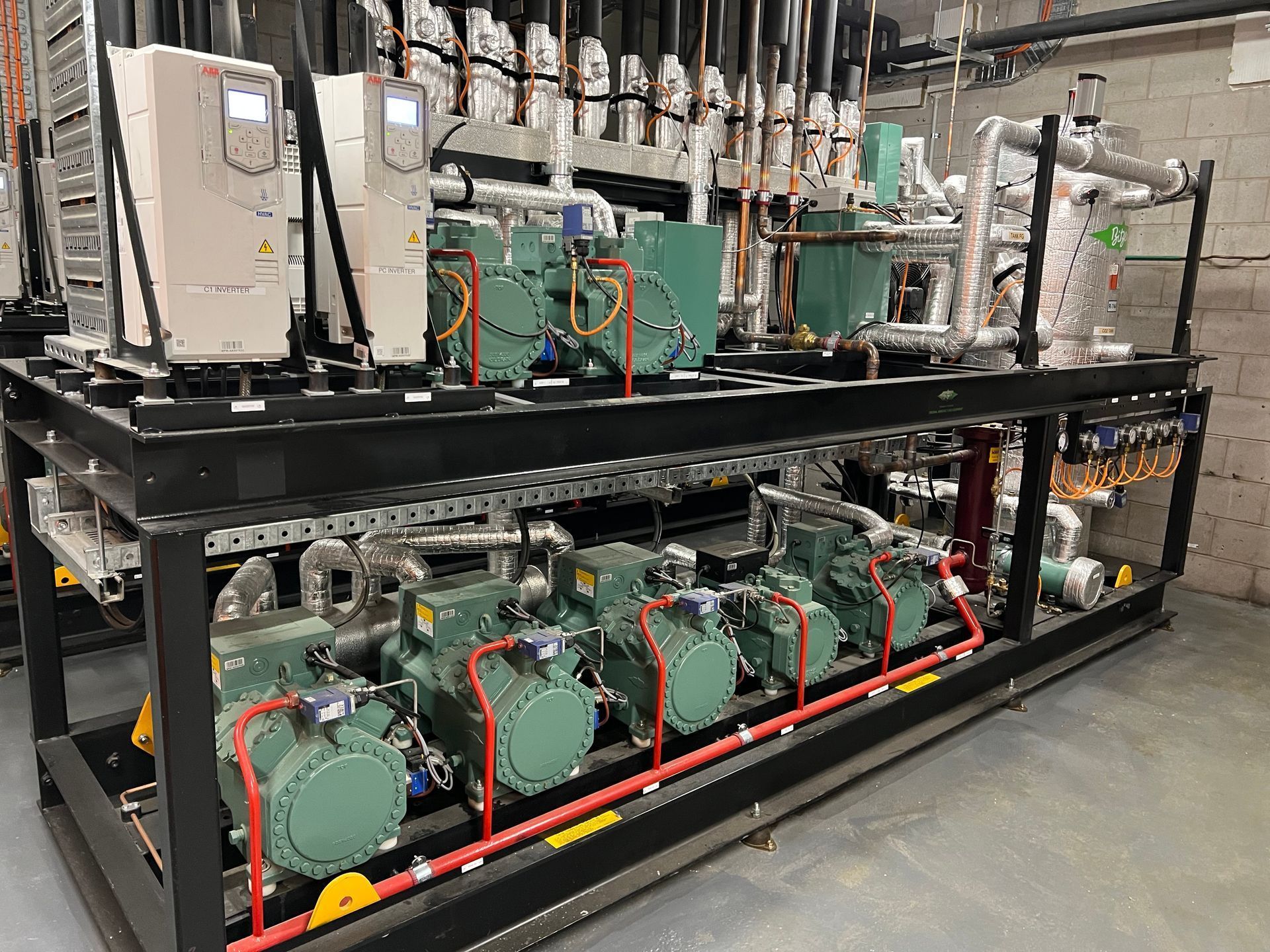 Industrial refrigeration equipment on a black metal rack in a factory setting, with green compressors and pipes.
