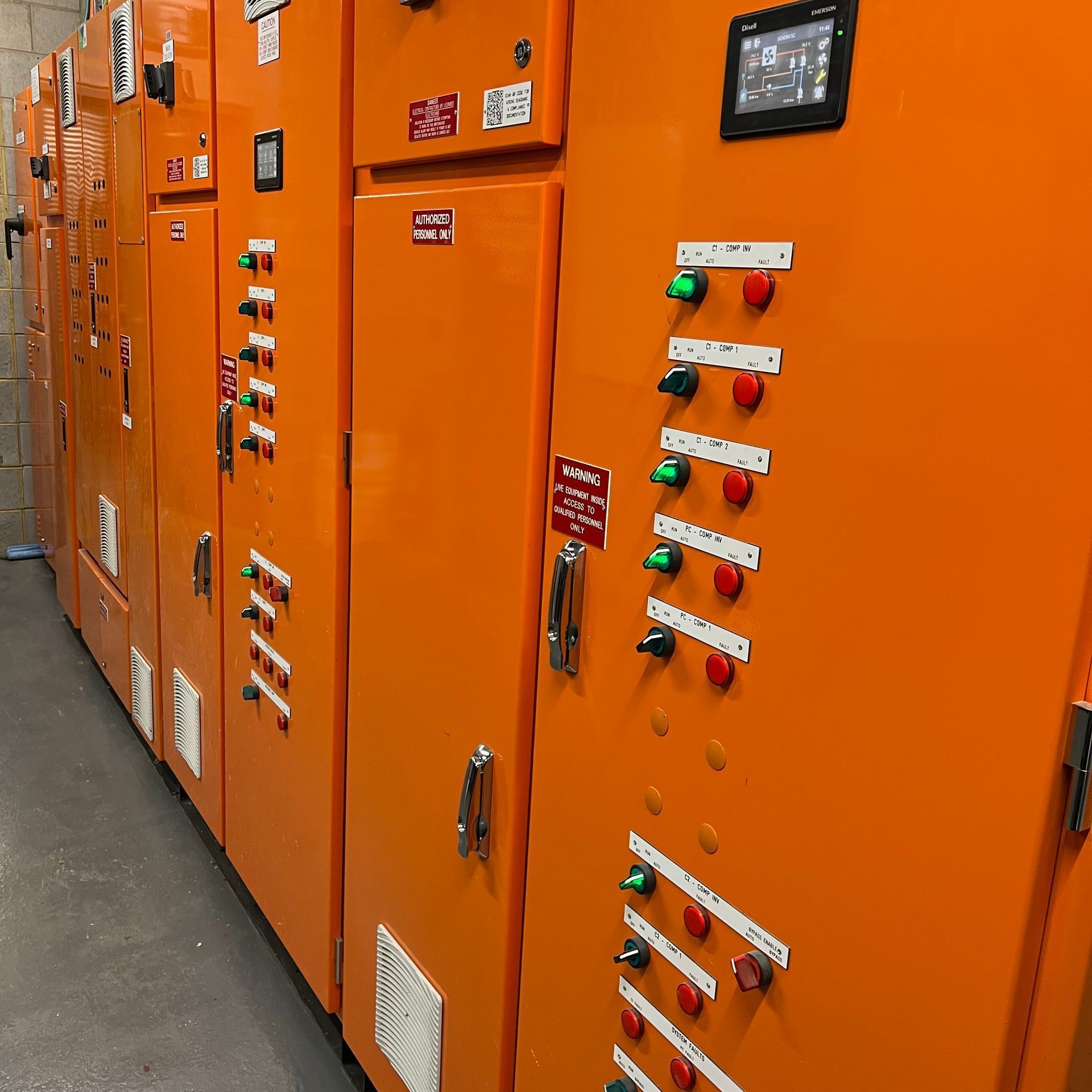 Orange electrical control cabinets with rows of switches and indicator lights in an industrial room