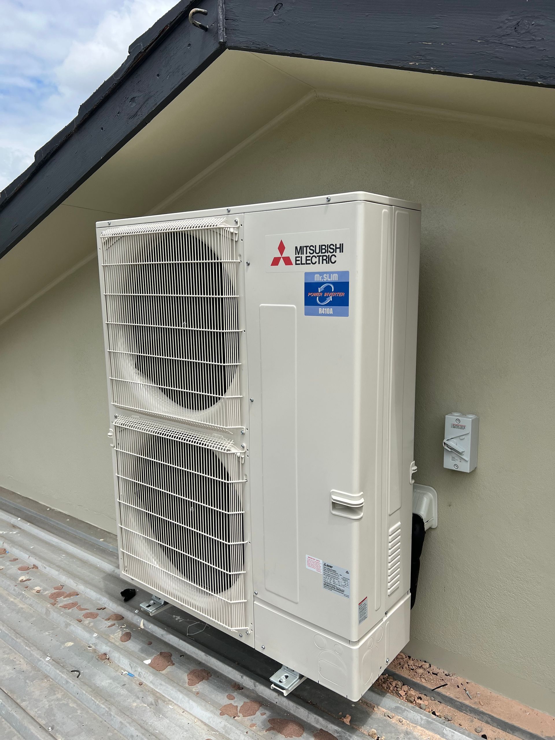 Outdoor air conditioner unit mounted on a wall beside a building roofline
