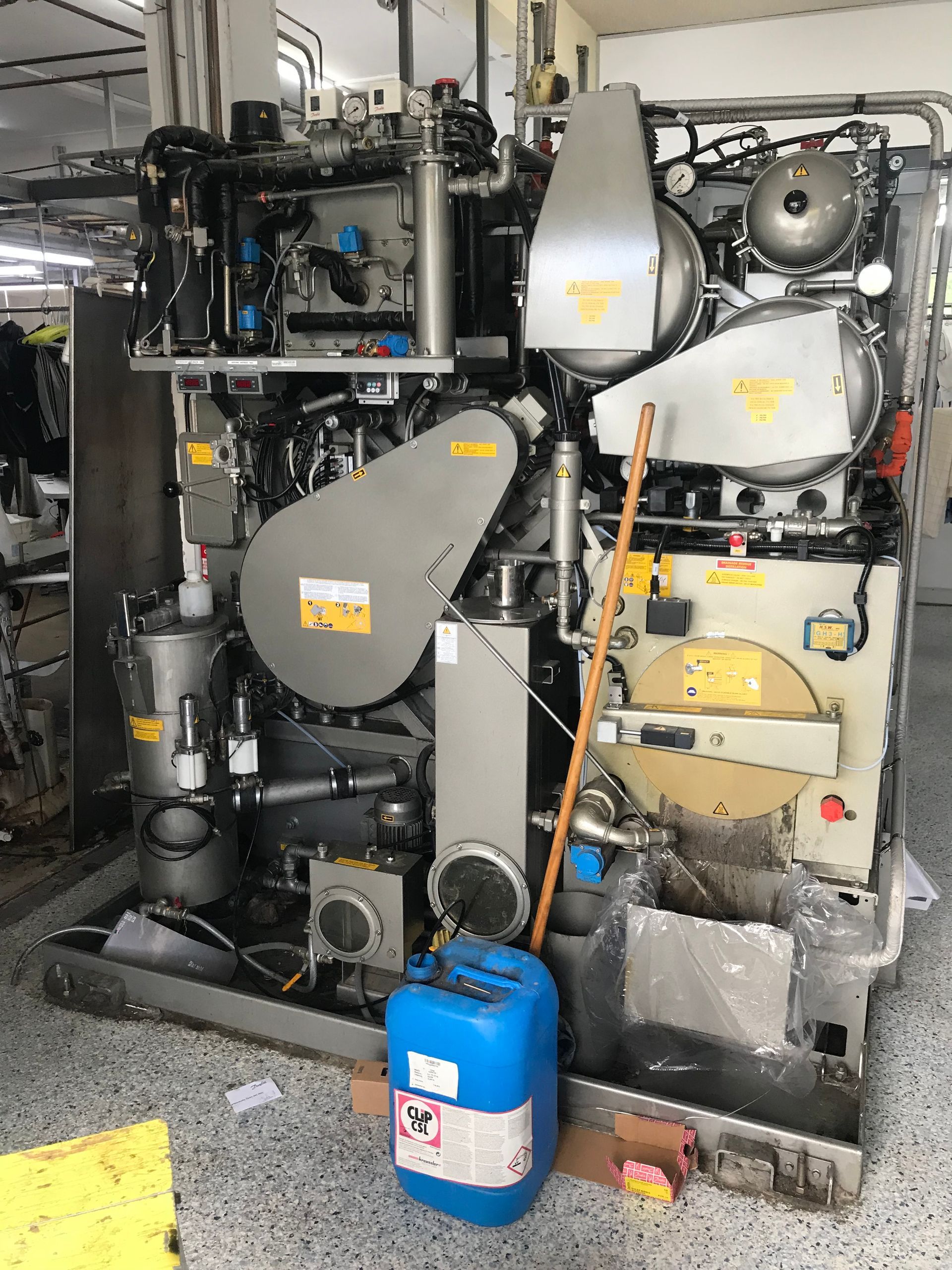 Industrial machinery with gray panels and tubing in a cluttered mechanical room, with a blue gas cylinder in front