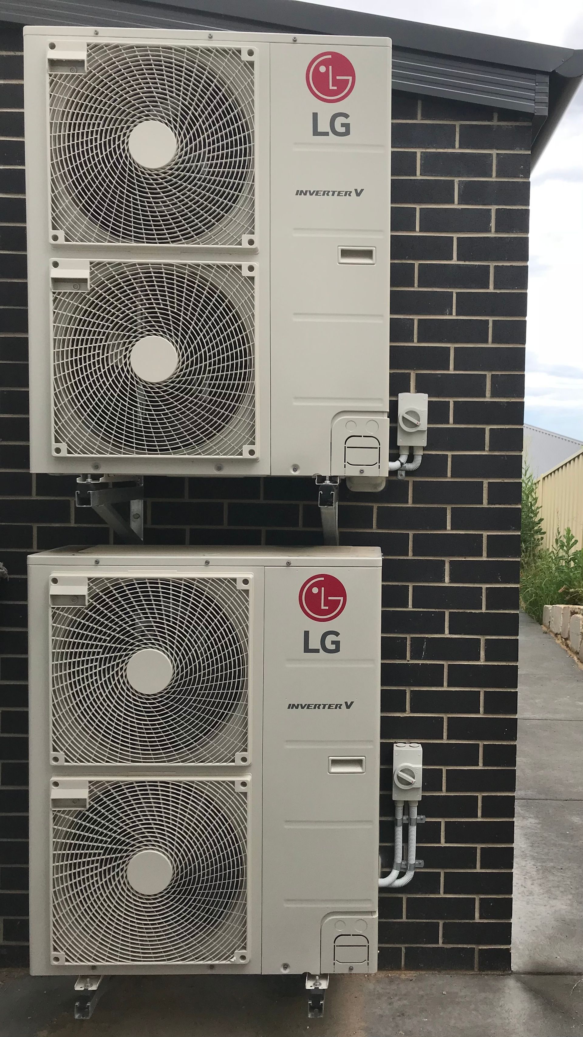 Two LG outdoor AC condenser units mounted on a brick wall, with three fans visible.