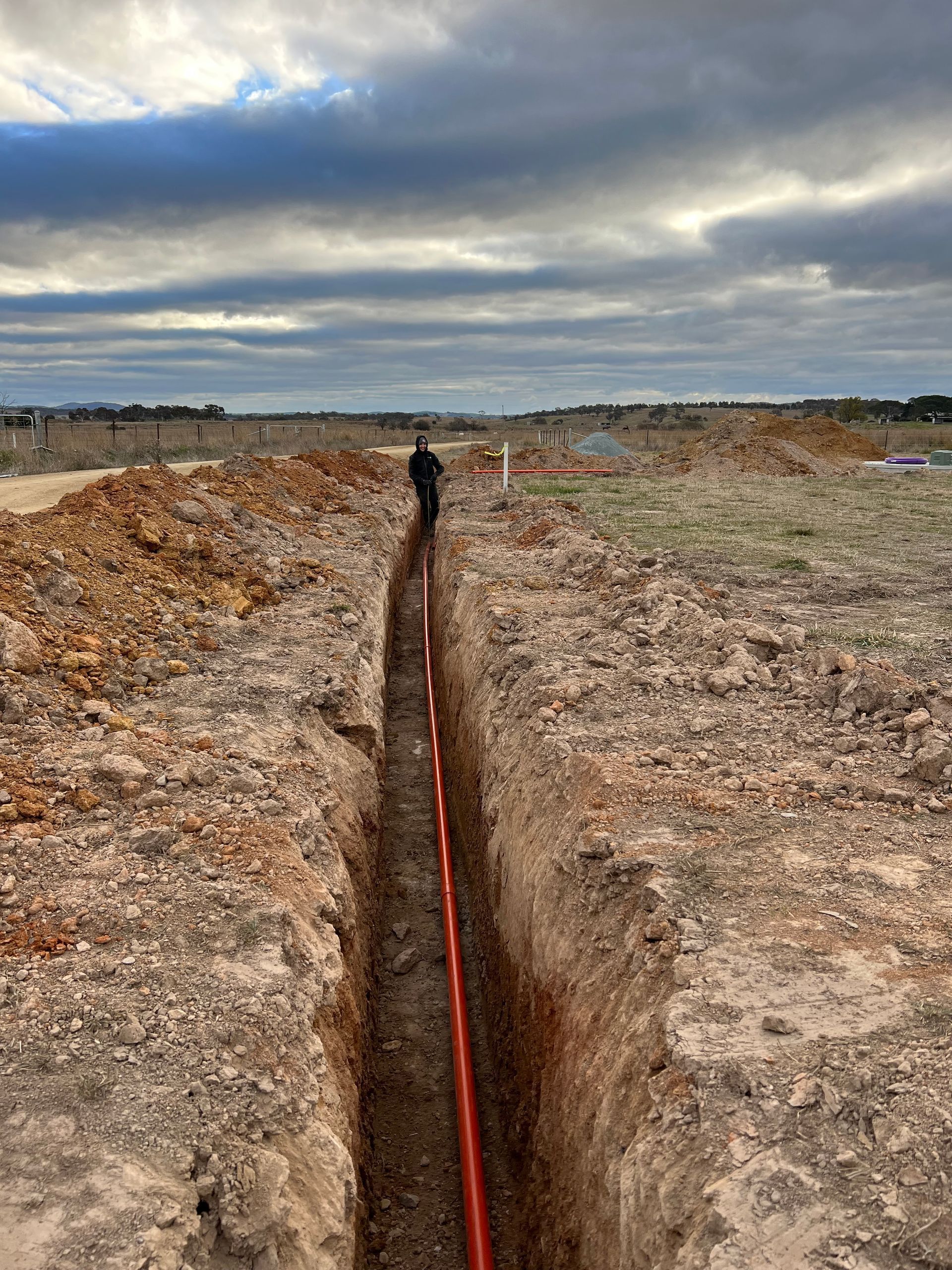A long trench in a barren field with a red cable running through it under a cloudy sky