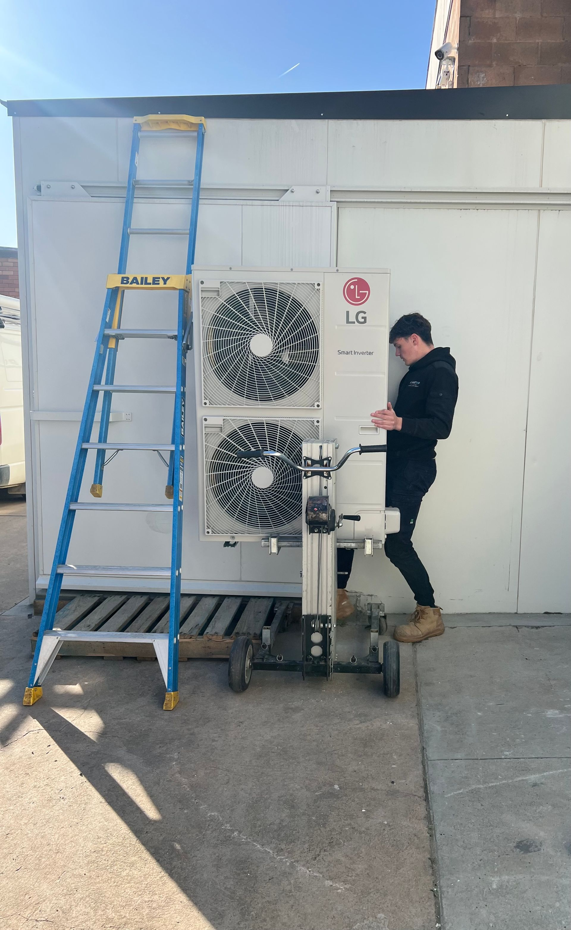 Worker adjusting rooftop HVAC units beside a blue ladder on an exterior wall
