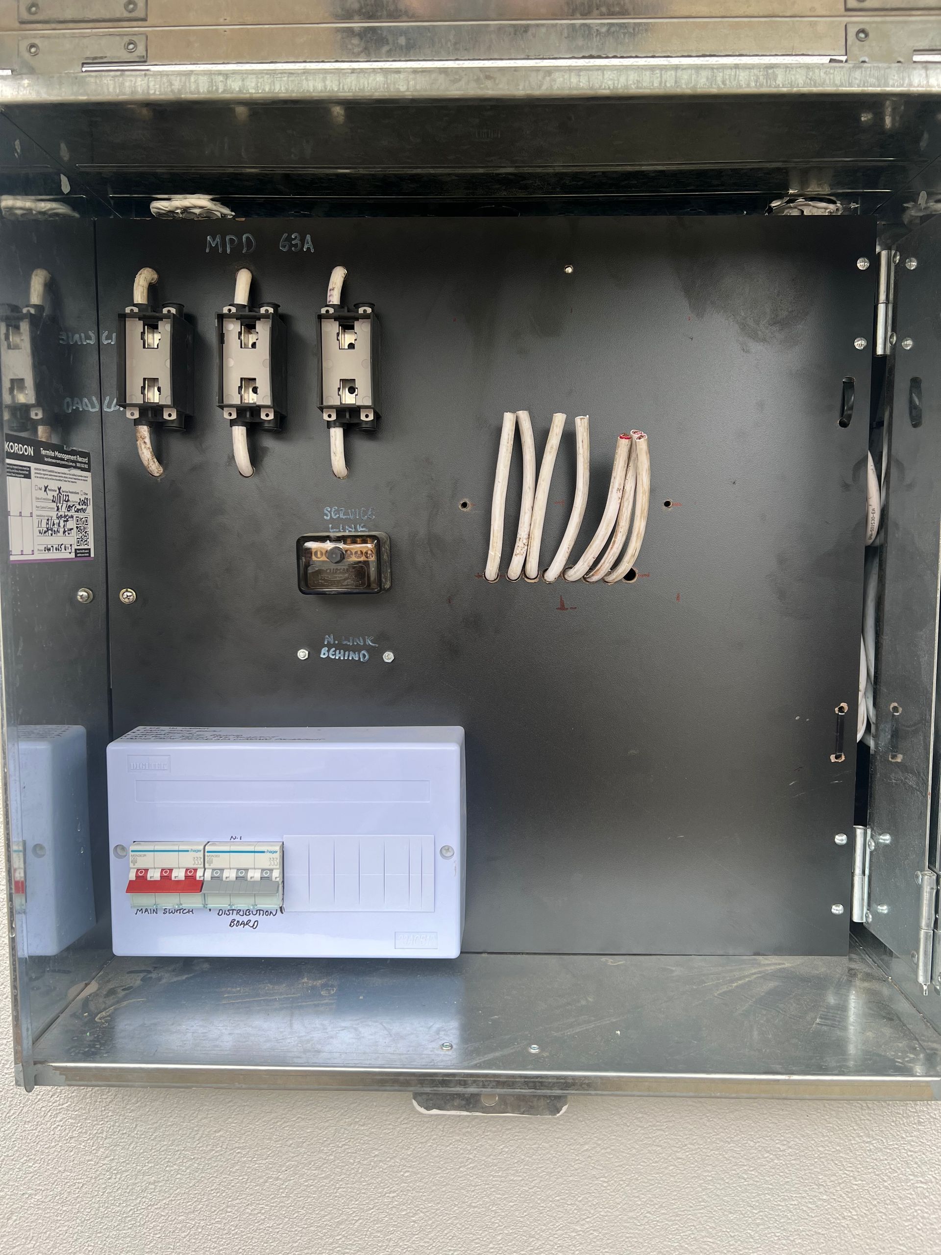 Open electrical cabinet with wiring, breakers, and a gray control box inside.