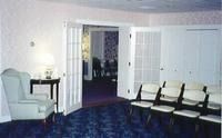 Empty living room with blue carpet, white walls, and chairs lined along the right side.