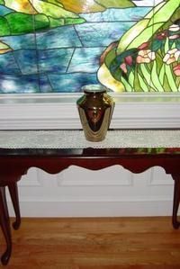 Decorative urn on a small table in front of a stained-glass window